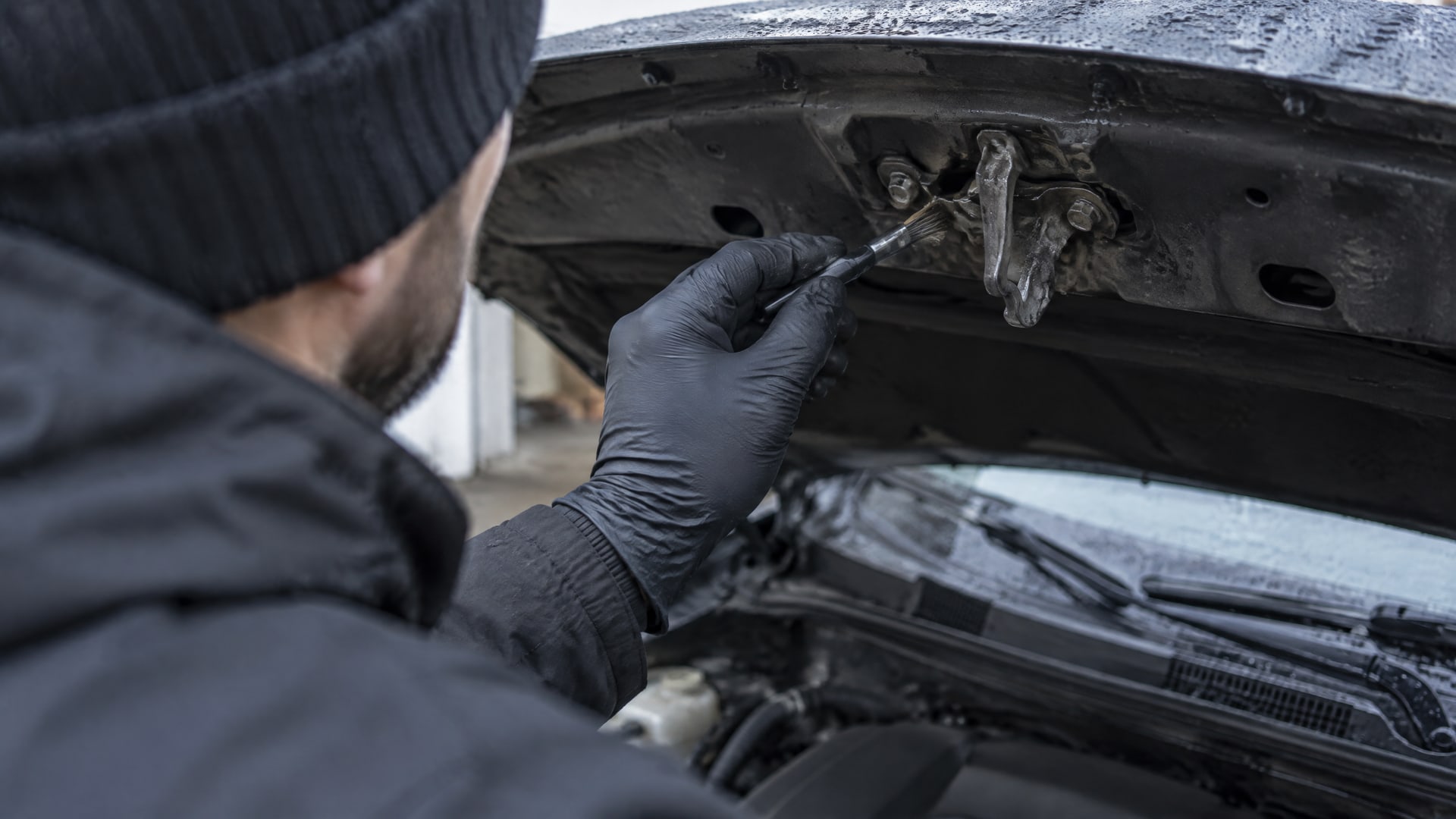 Рука в перчатке наносит wd-40 на шарниры и пины защелки капота автомобиля.